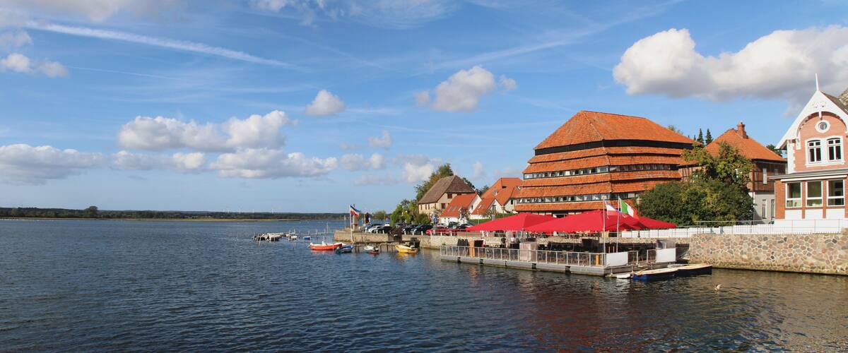 A lakeside town with traditional buildings, a dock with boats, and a clear sky.