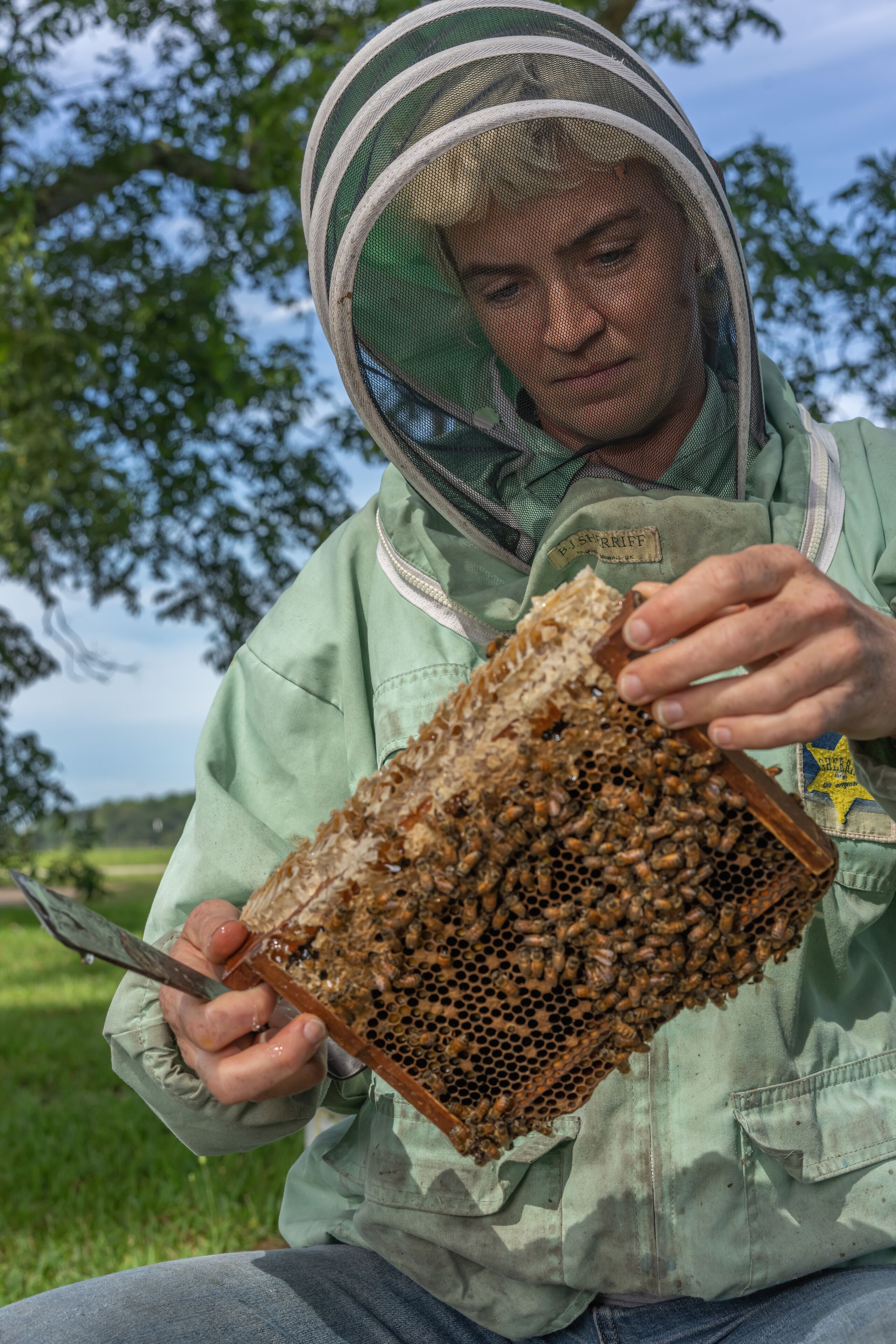 A person in a green jacket and protective headgear holding a honeycomb.