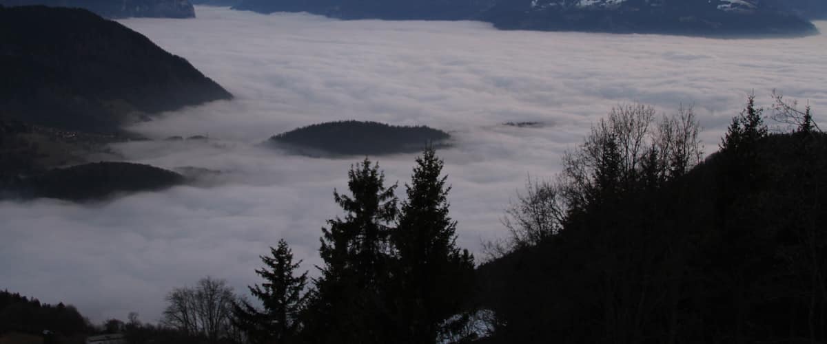 Snow-capped mountains, a valley with clouds, and a forested area.