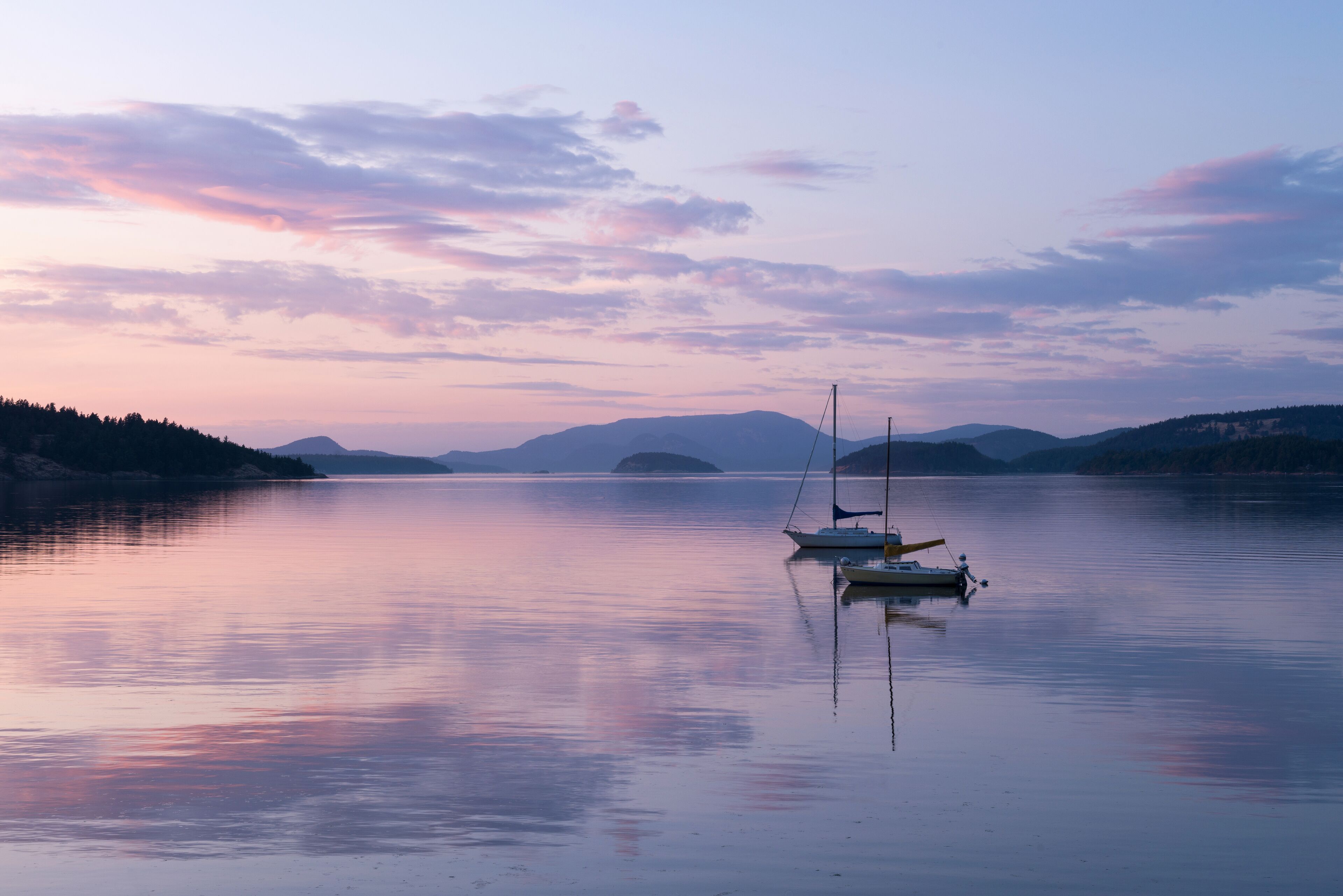 A calm lake with a sailboat anchored near the shore, surrounded by hills and a clear sky.