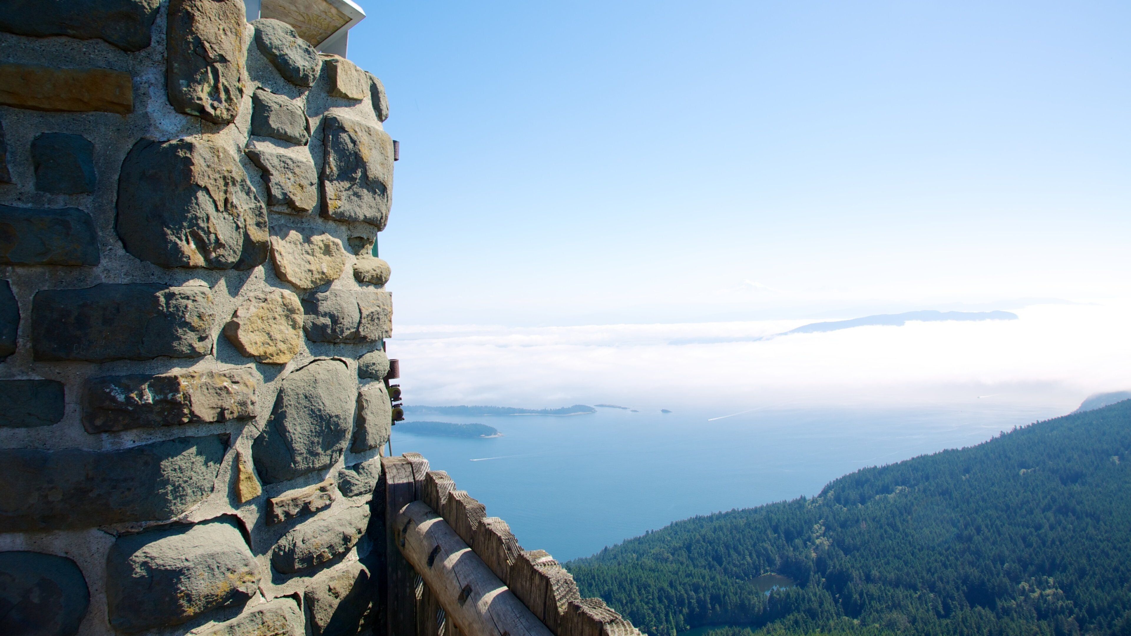 A stone wall overlooking a body of water with a forested mountain in the background.