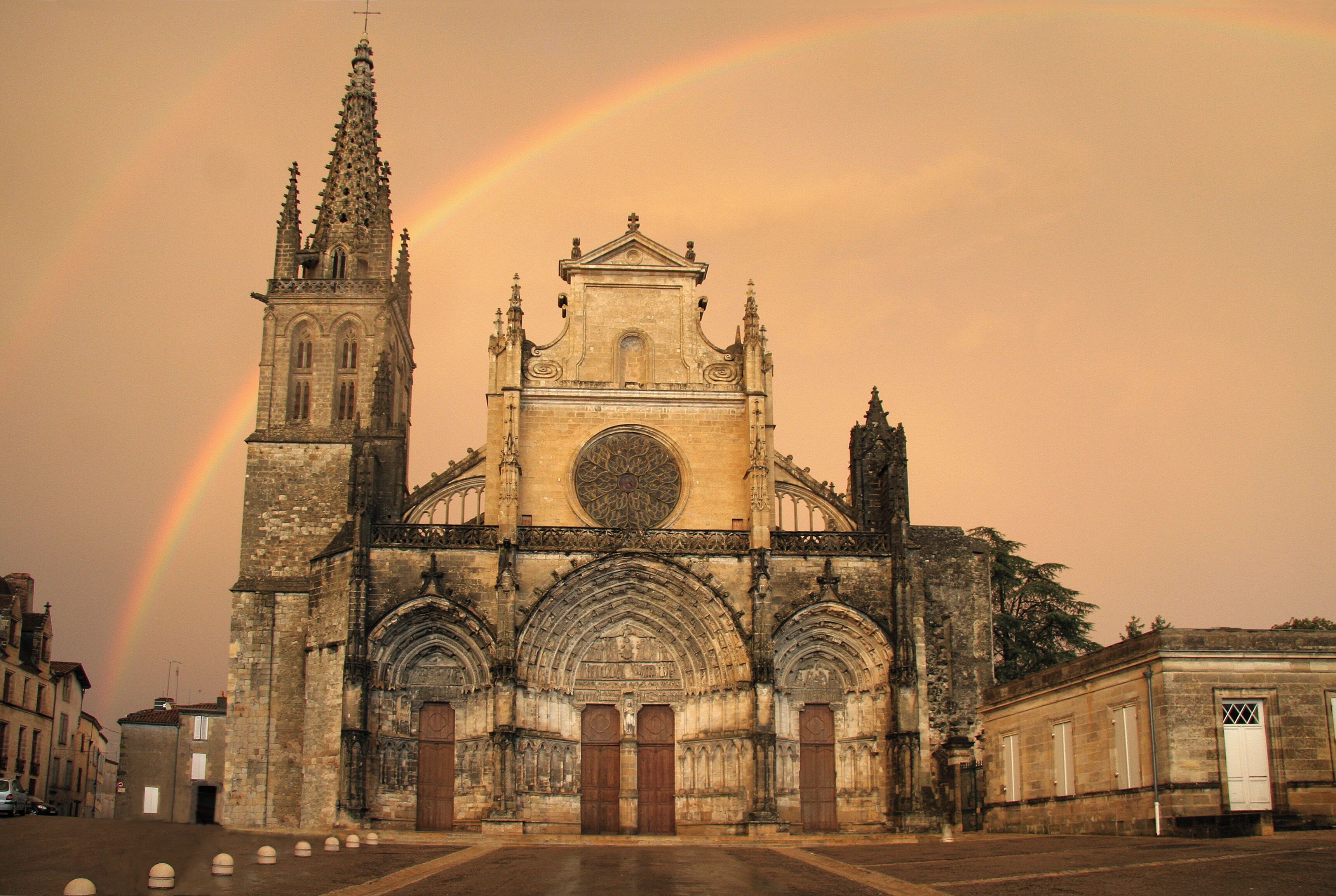 A cathedral with a large rose window and a tall spire, under a rainbow.