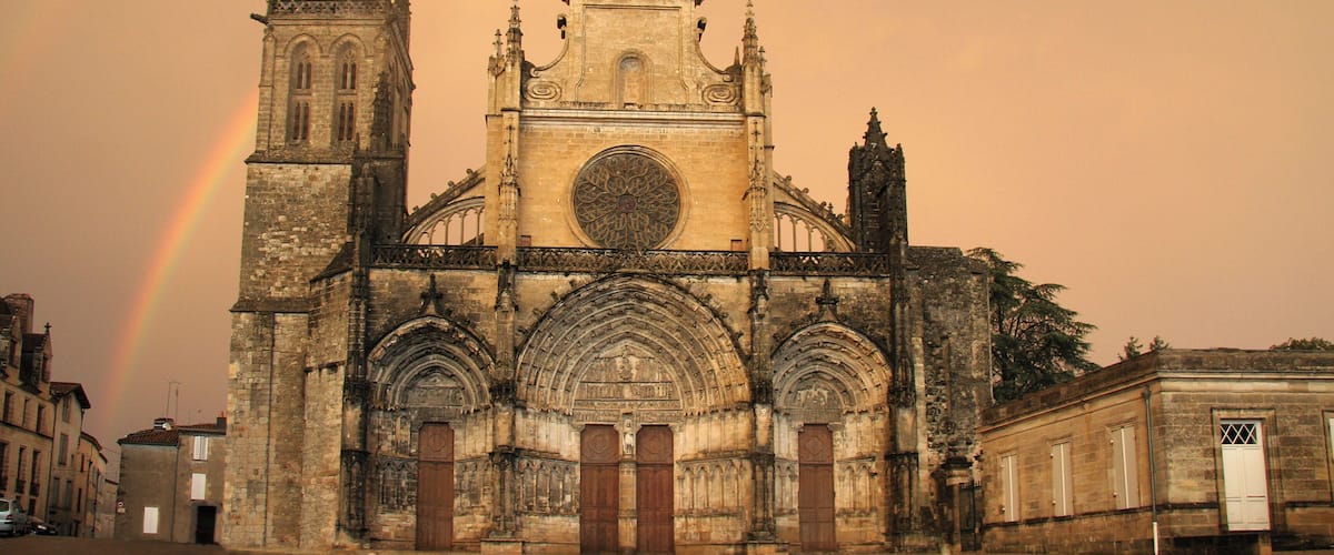 A cathedral with a large rose window and a tall spire, under a rainbow.