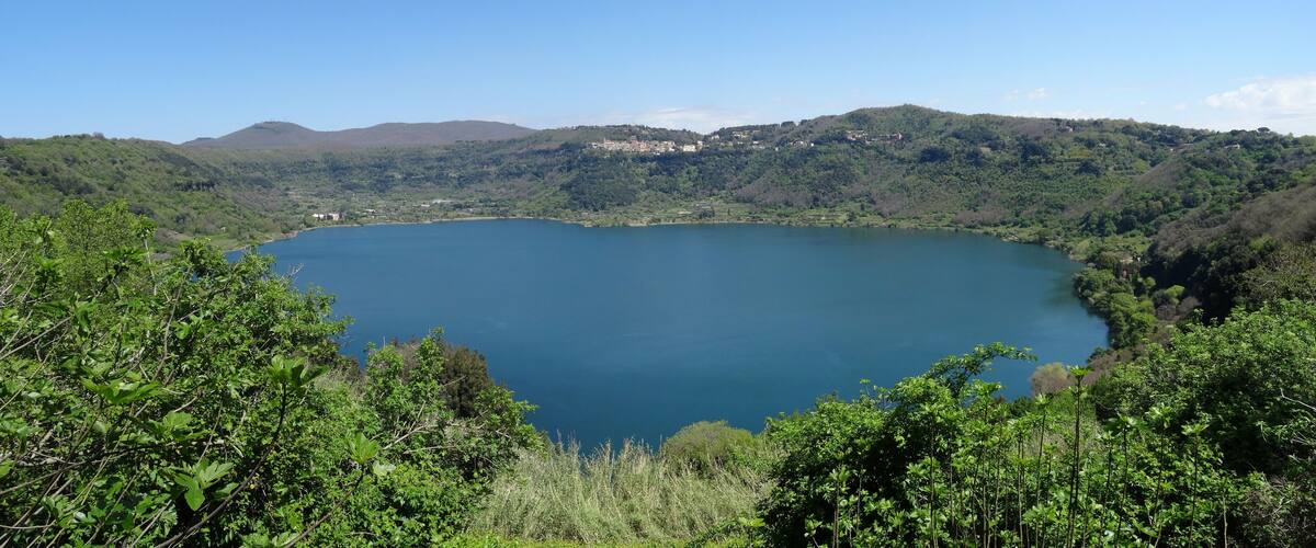 A large lake surrounded by lush green hills and a few scattered buildings.