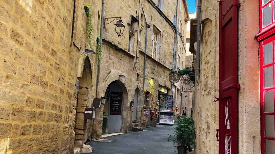 A narrow street with stone buildings, a red door, and a sign for 'CERAMIC ARTS'.