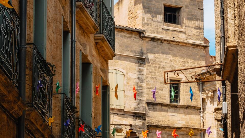 A narrow street with colorful pinwheel decorations and a historic bell tower.