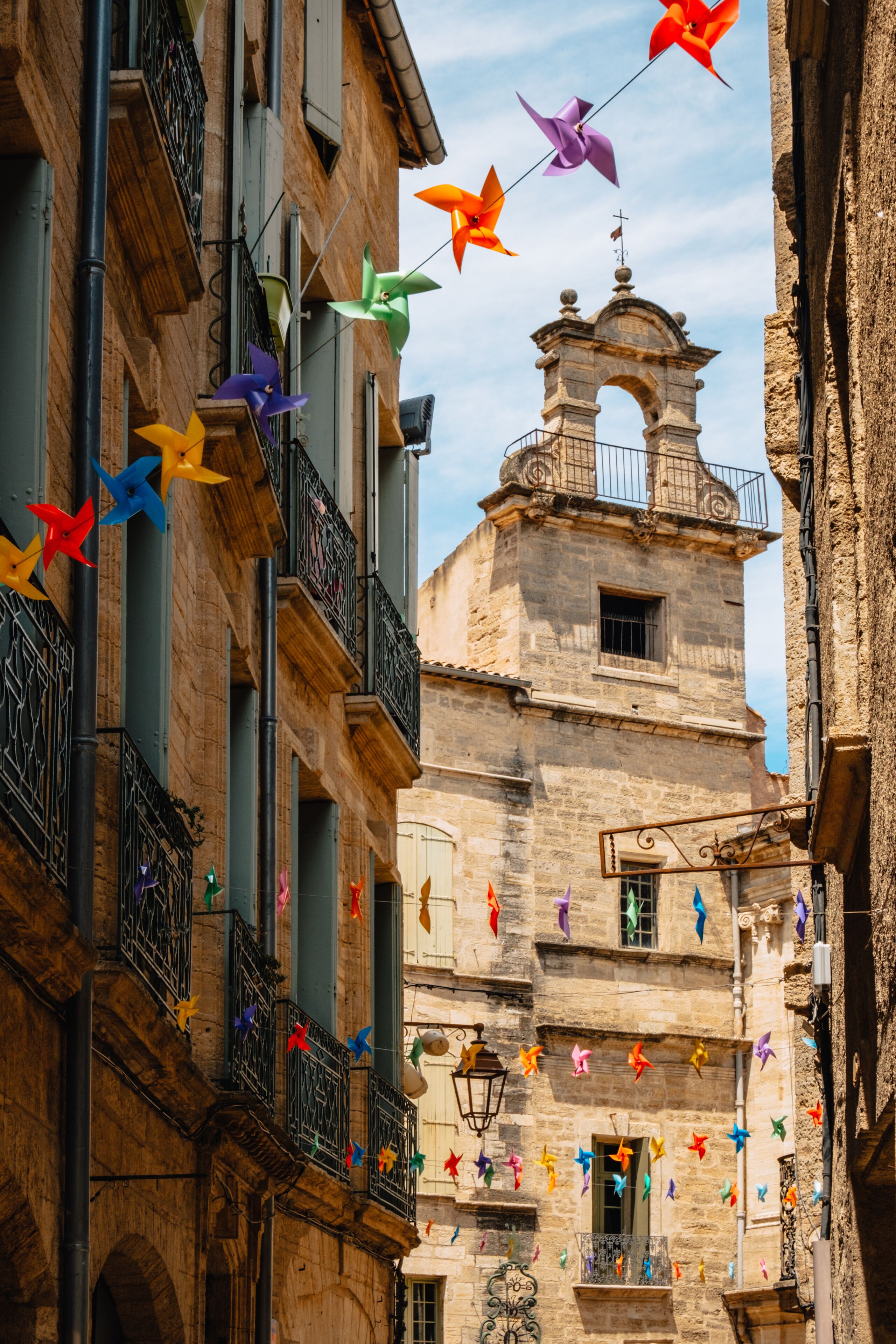 A narrow street with colorful pinwheel decorations and a historic bell tower.