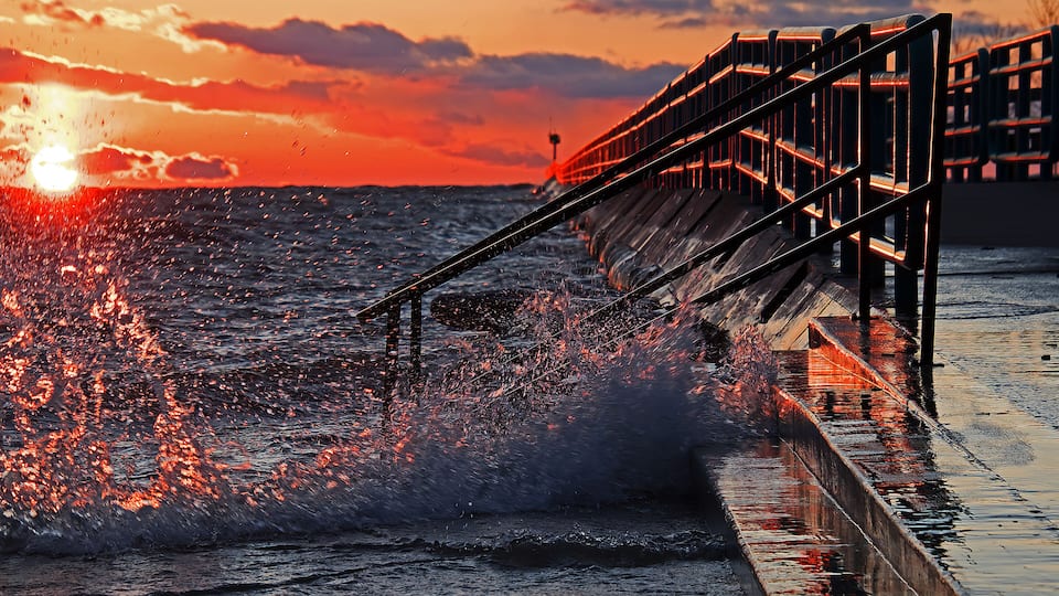 A pier extending into the ocean at sunset with waves crashing against it.
