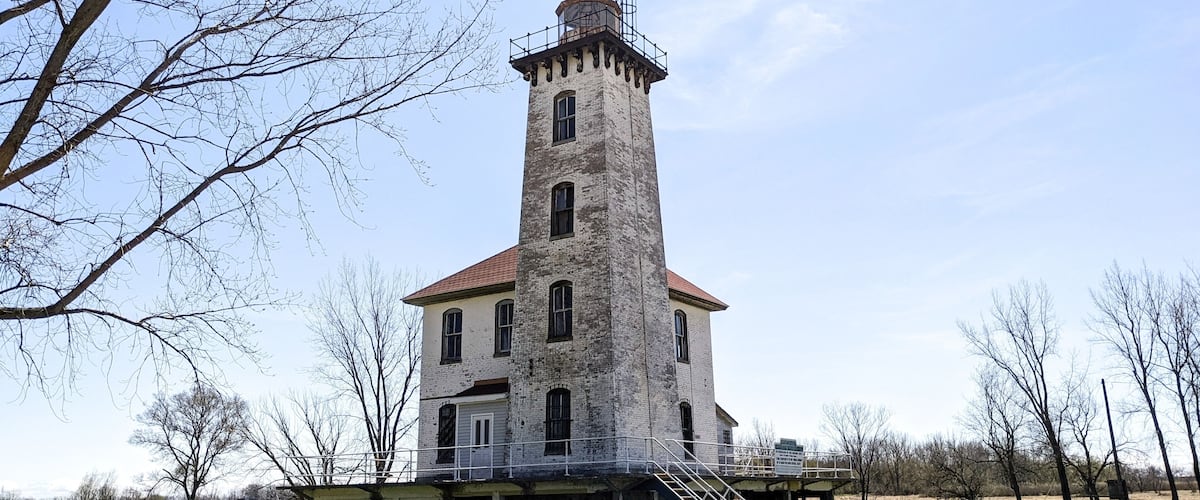 A historic tower with a red roof and white walls, surrounded by a grassy area and leafless trees.