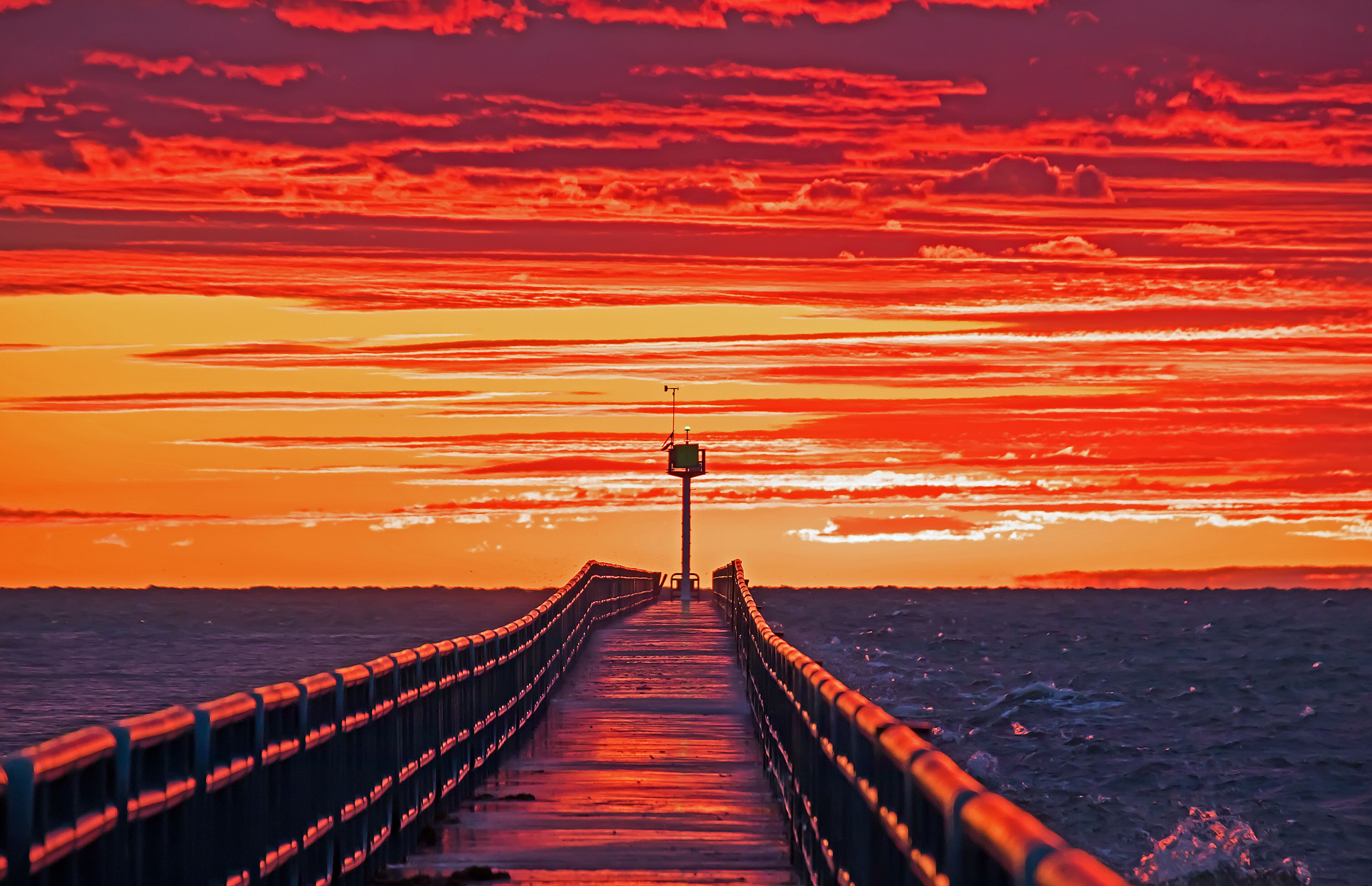 A pier extending into the ocean with a sunset in the background.