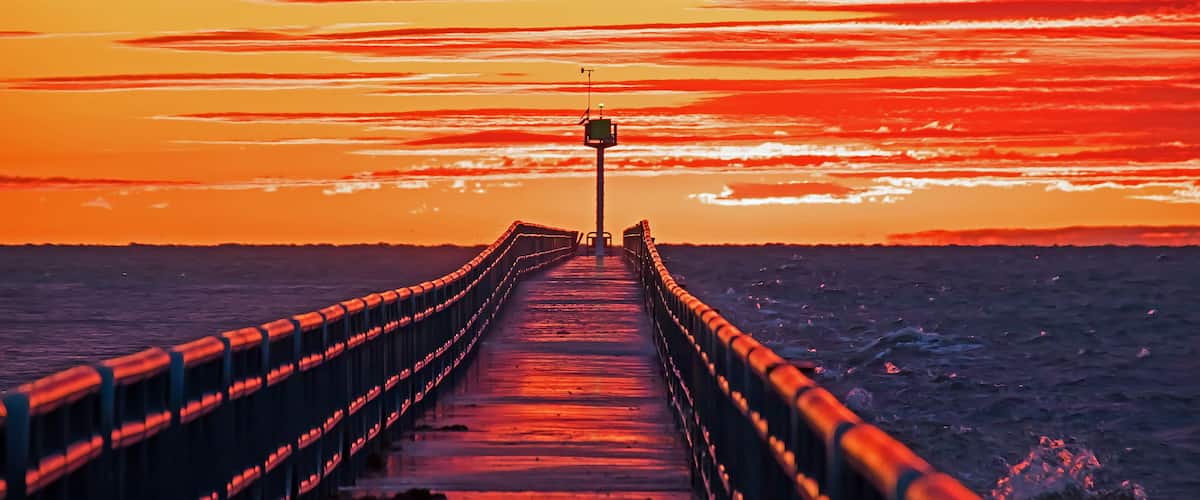 A pier extending into the ocean with a sunset in the background.