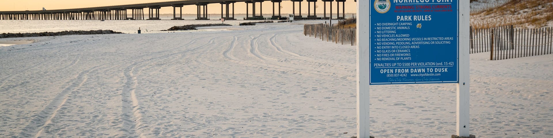 A snowy beach with a pier in the background and a sign listing Norriego Point park rules.