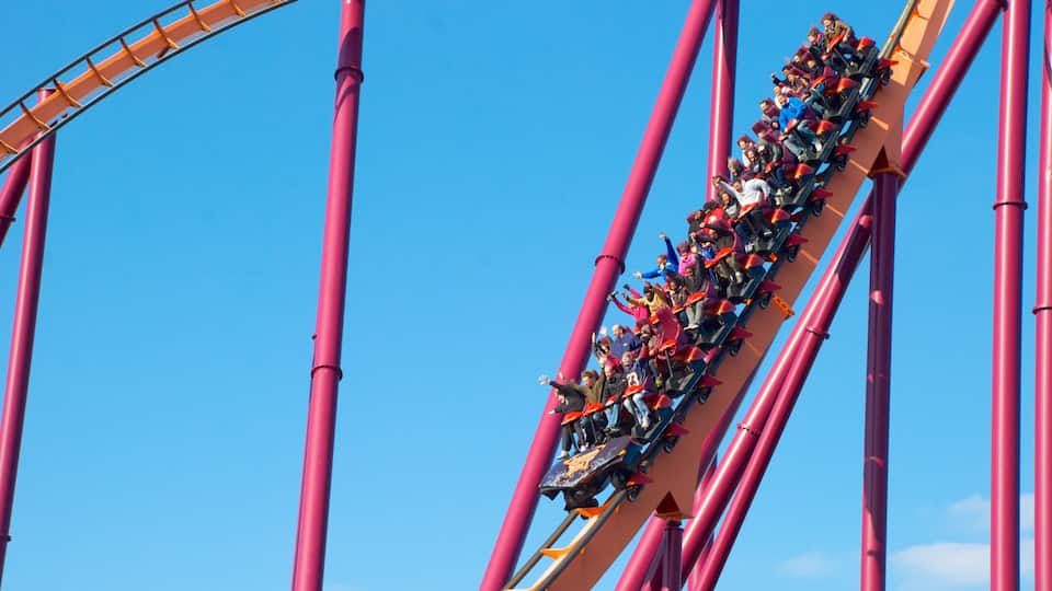 A roller coaster with riders in red cars.