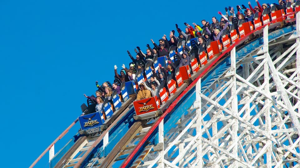A roller coaster with riders in mid-ride, a clear blue sky, and a wooden structure.
