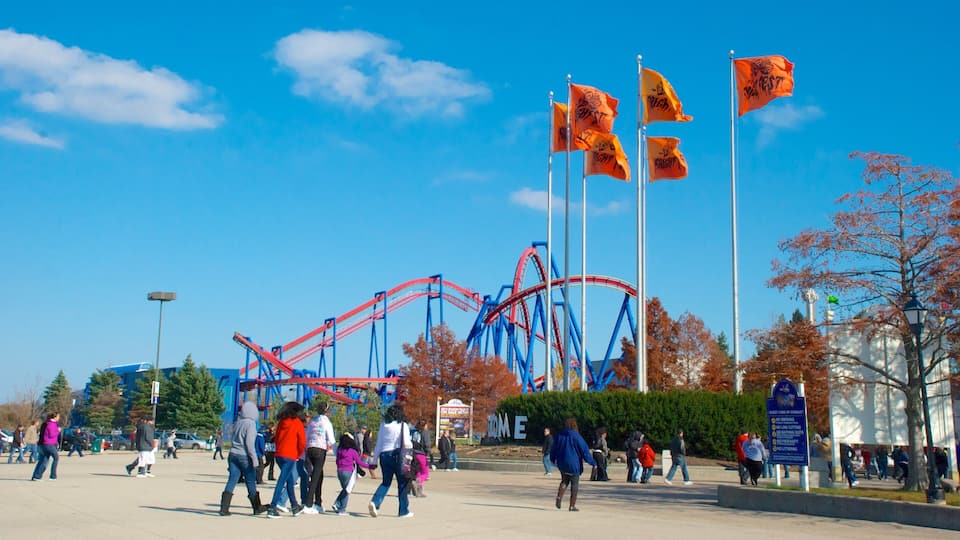 A roller coaster, flags, and people walking in an outdoor area.