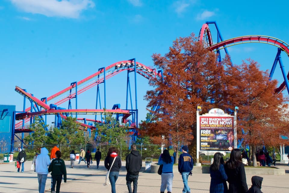 A roller coaster at an amusement park with autumn trees and a clear blue sky.