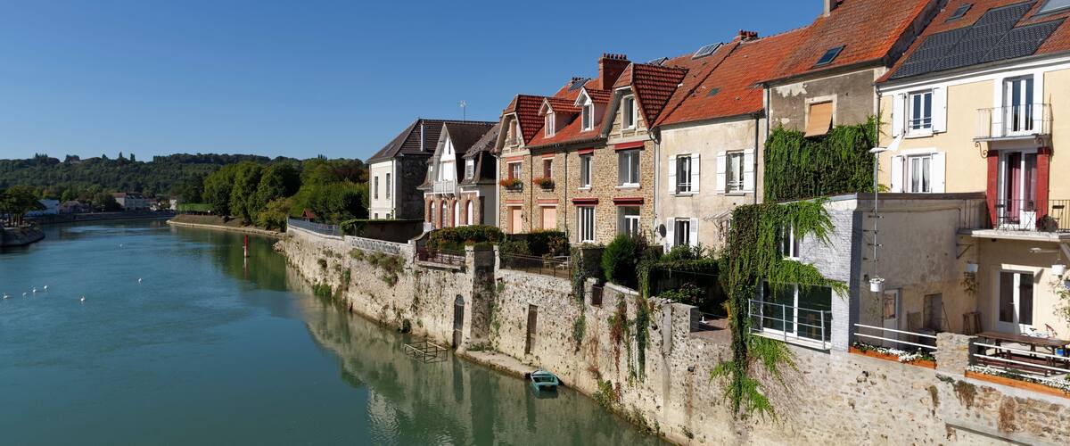 A river with houses along the banks, a stone wall, and a clear blue sky.