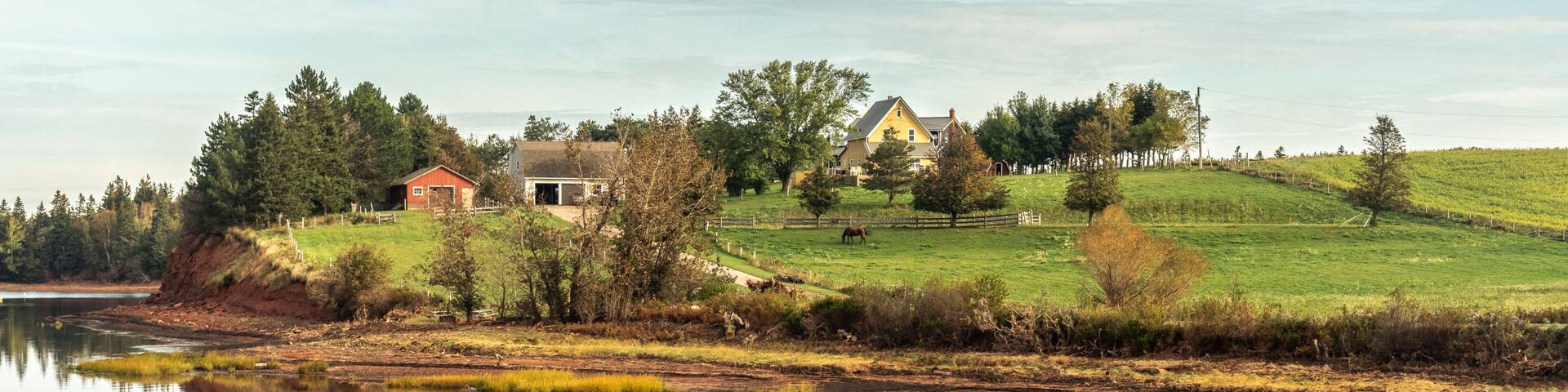 A small village on the edge of a peninsula with trees and houses reflecting in the calm bay water, Prince Edward Island, Canada