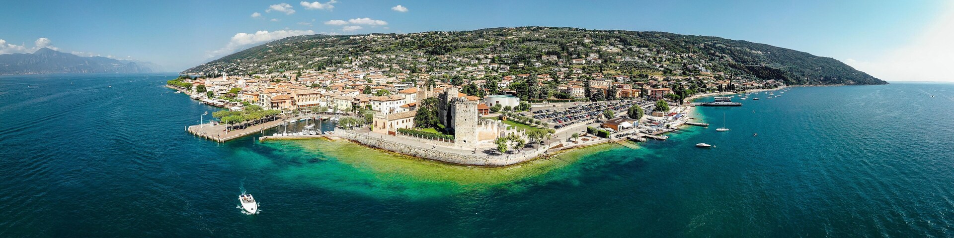 A coastal town with a prominent castle, clear blue waters, and a hilly landscape in the background.