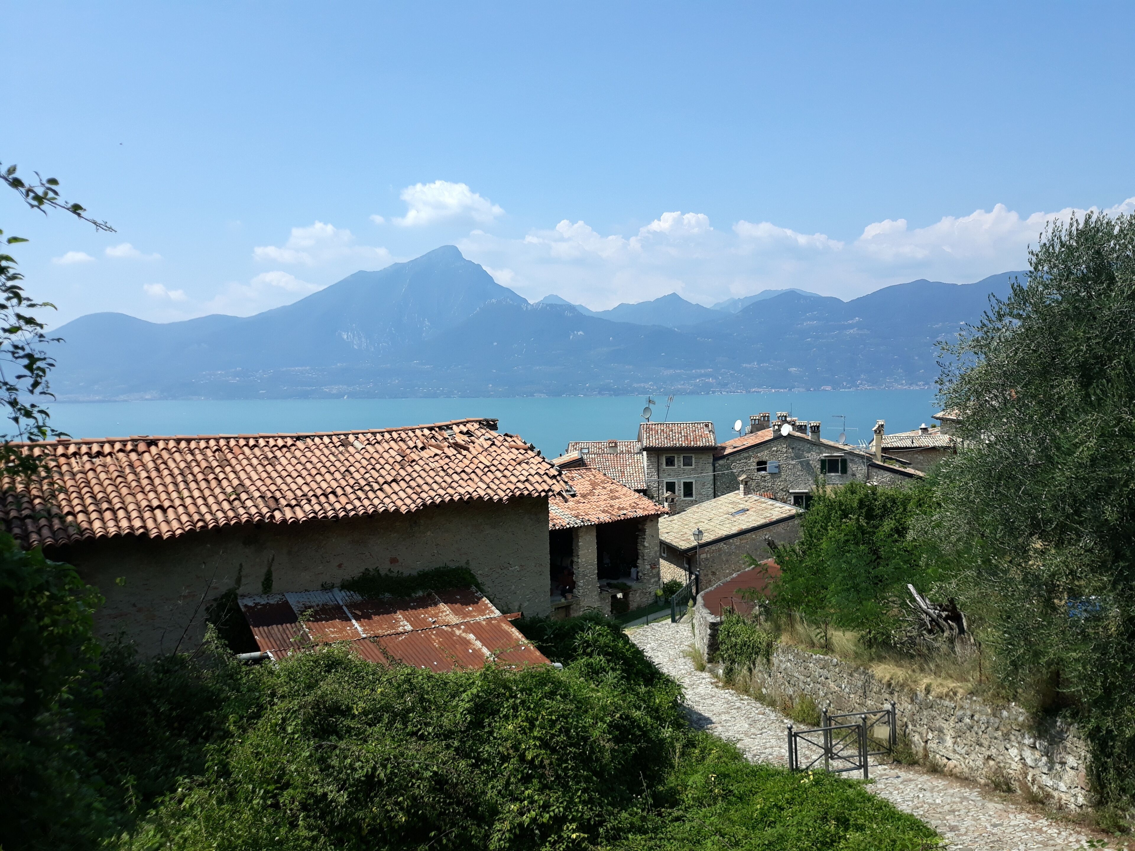 A coastal village with terracotta-roofed buildings, a stone pathway, and a mountain in the background.
