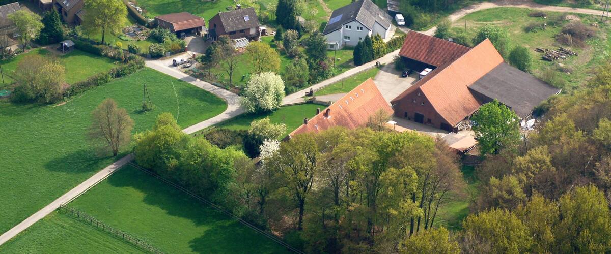 An aerial view of a rural village with houses, green fields, and a winding road.
