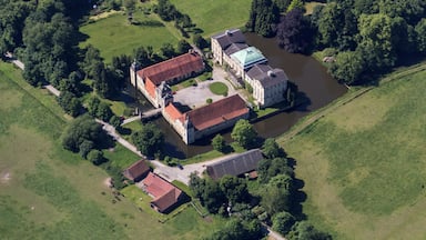 Vue aérienne d’un domaine historique doté d’une vaste cour, d’une rivière et d’une végétation luxuriante environnante.