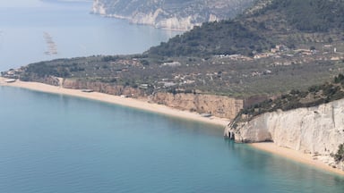 Paisagem costeira com uma praia de areia, falésias e uma cidade ao fundo.
