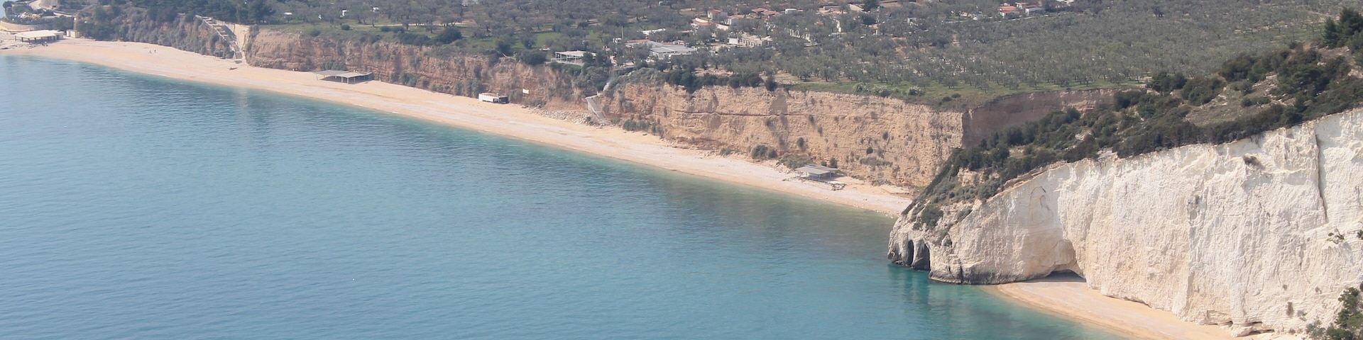 Un paisaje costero con una playa arenosa, acantilados y un pueblo al fondo.