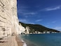 A coastal cliff with a beach and clear blue sea.