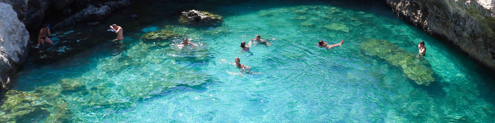 A clear blue pool surrounded by rocky cliffs with people swimming.