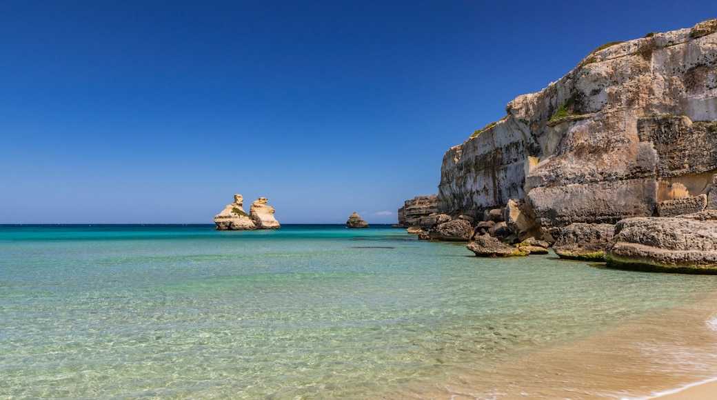 A clear turquoise sea, a sandy beach, and rocky cliffs.