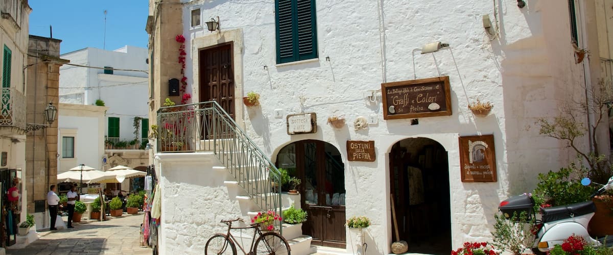 A narrow street with white buildings, a bicycle, and potted plants.