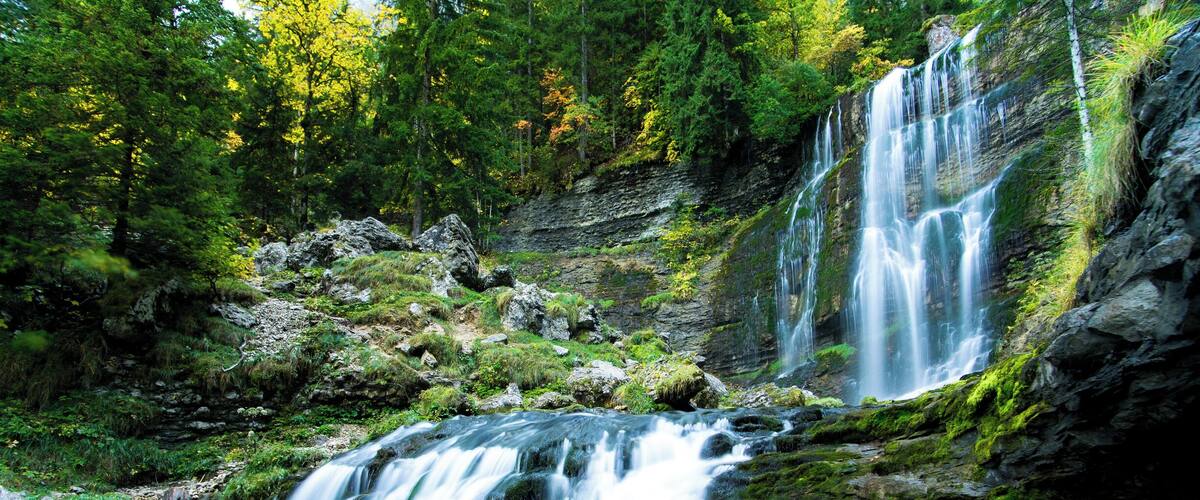 A waterfall cascading over moss-covered rocks in a forested area.