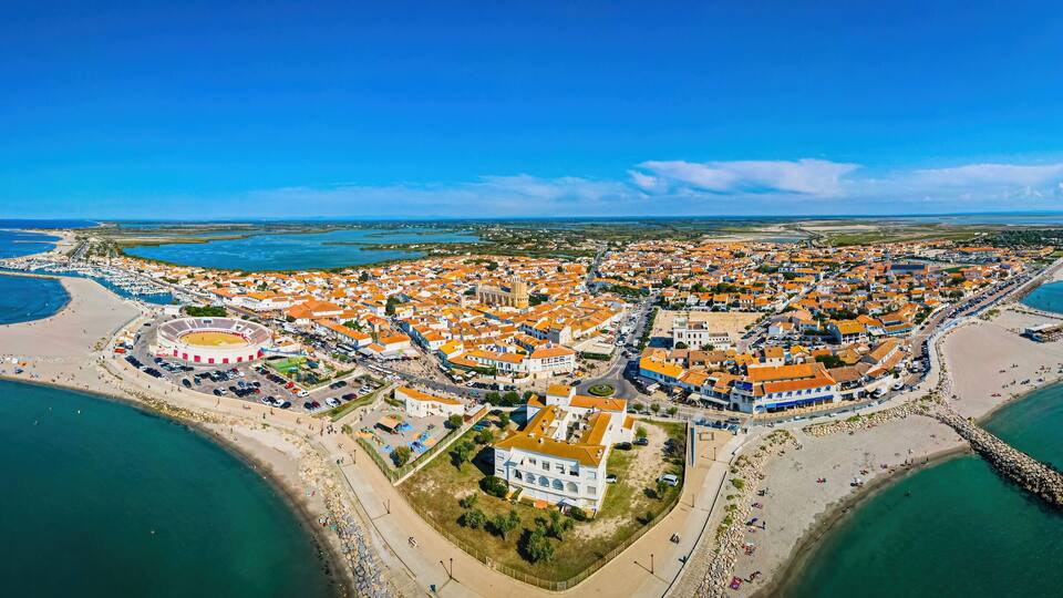 An aerial view of a coastal town with a central plaza, a stadium, and a beach.