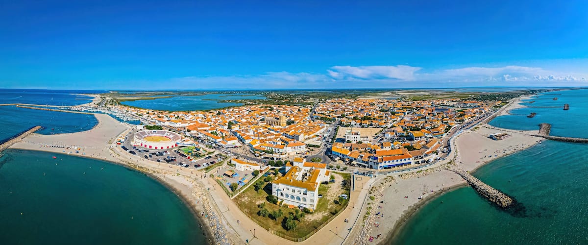 An aerial view of a coastal town with a central plaza, a stadium, and a beach.