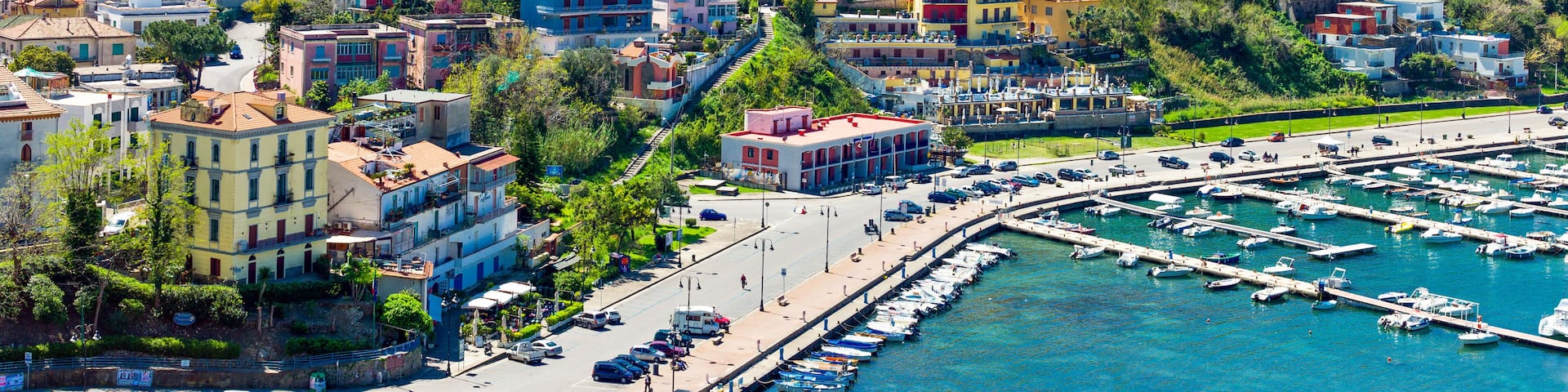 A coastal town with colorful buildings, a marina, and a hilly backdrop.