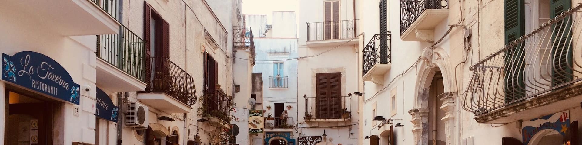 A narrow cobblestone street lined with buildings, outdoor seating at cafes, and a motorcycle parked on the side.