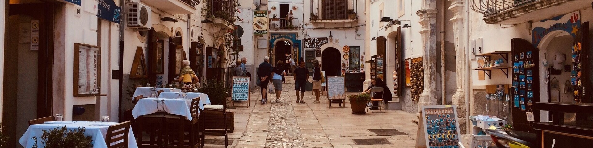 Una estrecha calle adoquinada bordeada de edificios, con mesas al aire libre en cafés y una motocicleta estacionada al costado.
