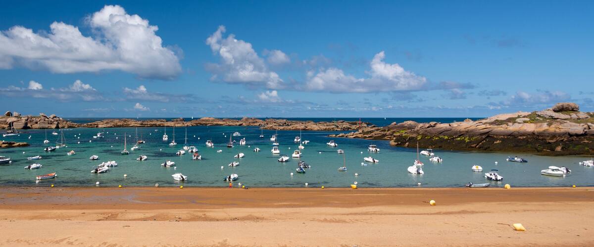 A rocky beach with numerous boats anchored in the water.
