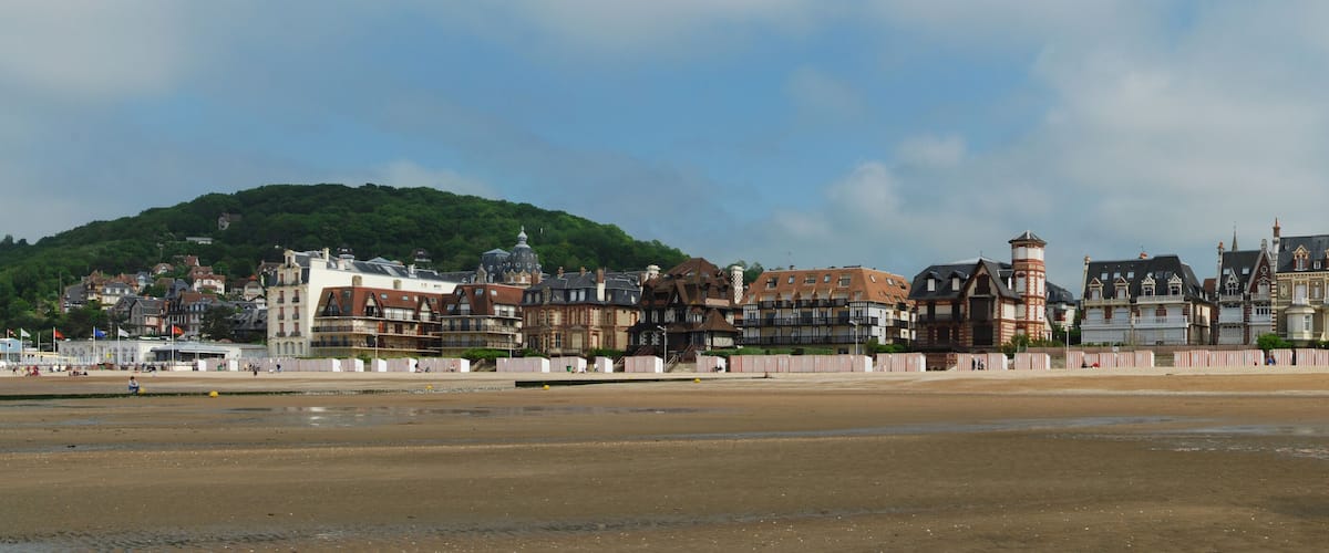 A coastal town with historic buildings, a sandy beach, and a hill in the background.