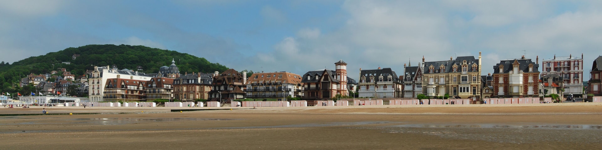 A coastal town with historic buildings, a sandy beach, and a hill in the background.