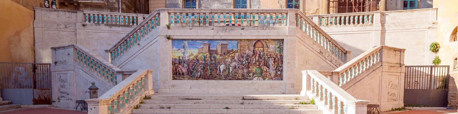 A grand staircase with a mural, leading to a historic building with classical architecture.