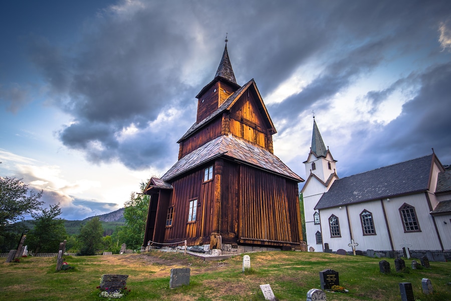 Una iglesia de madera con un campanario alto y un edificio más pequeño adyacente.