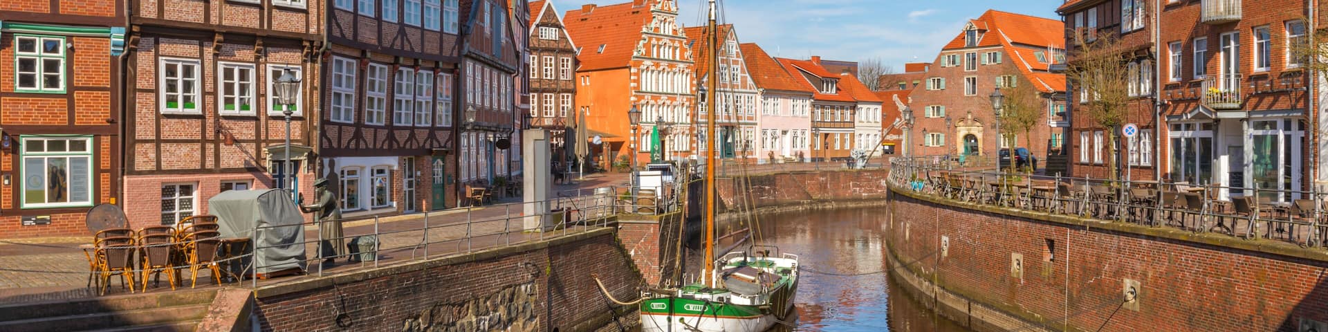 A narrow canal with a boat docked on the right, surrounded by historic buildings with red-tiled roofs and timber framing.