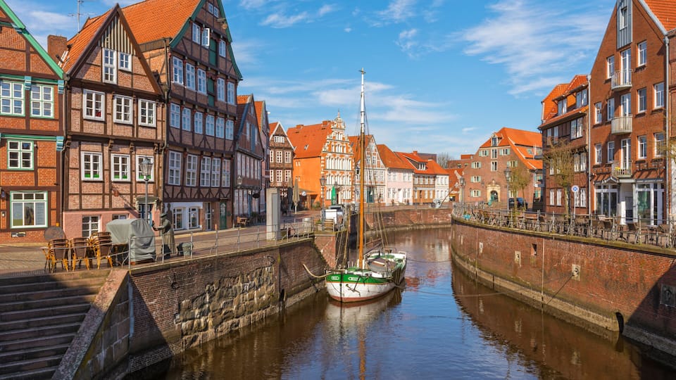 A narrow canal with a boat docked on the right, surrounded by historic buildings with red-tiled roofs and timber framing.