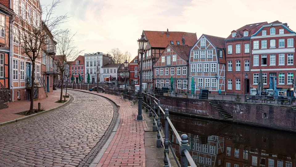 A cobblestone street lined with historic red brick buildings, a canal, and a bridge.
