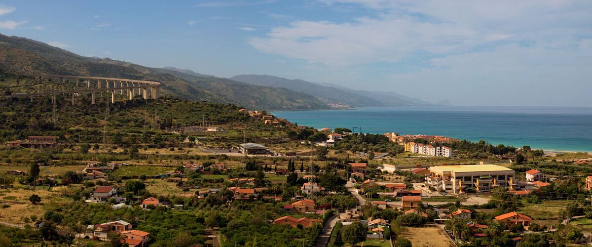 A coastal town with a bridge, houses, and a large building near the sea.