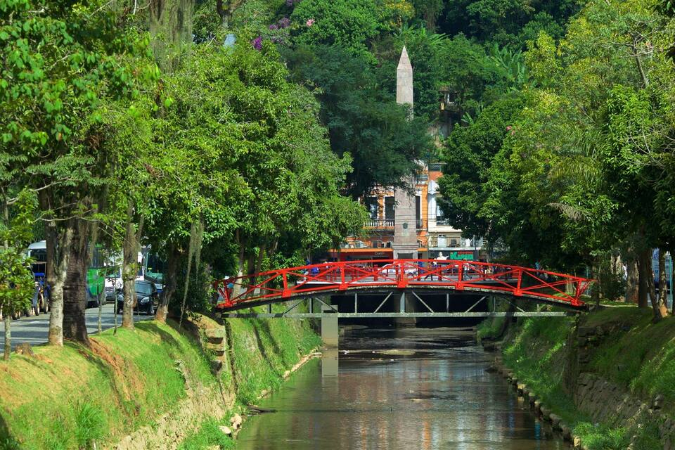 A red bridge over a canal with trees on either side.