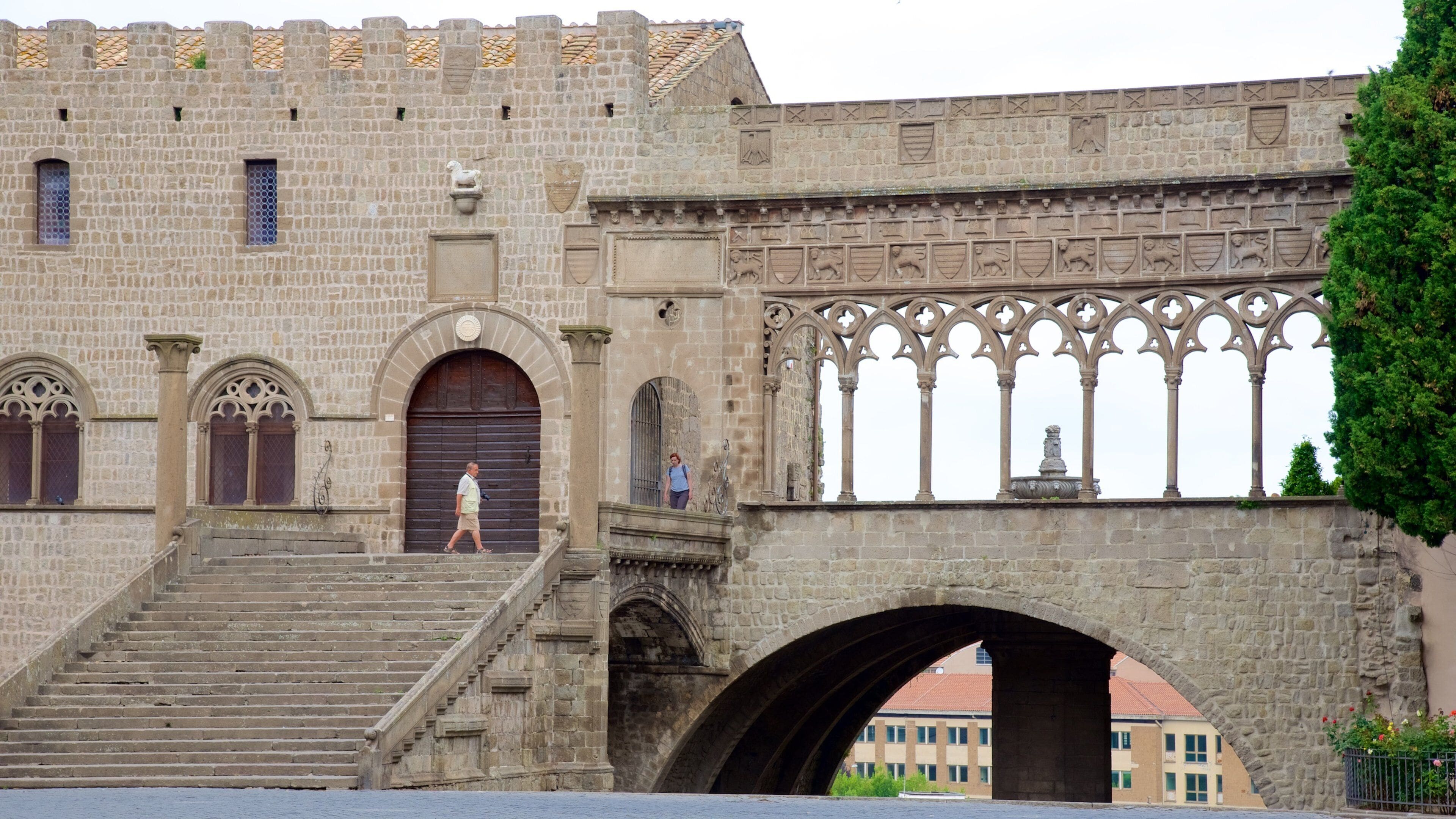 A historic stone building with arched windows and a large stone bridge with decorative metalwork.