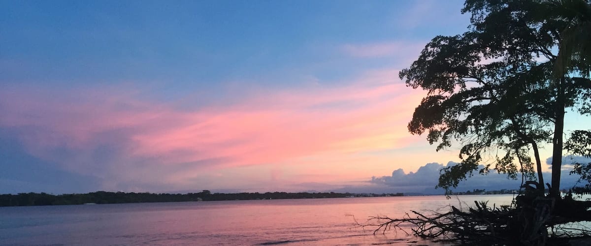 A sunset over a calm lake with a sandy beach and trees.